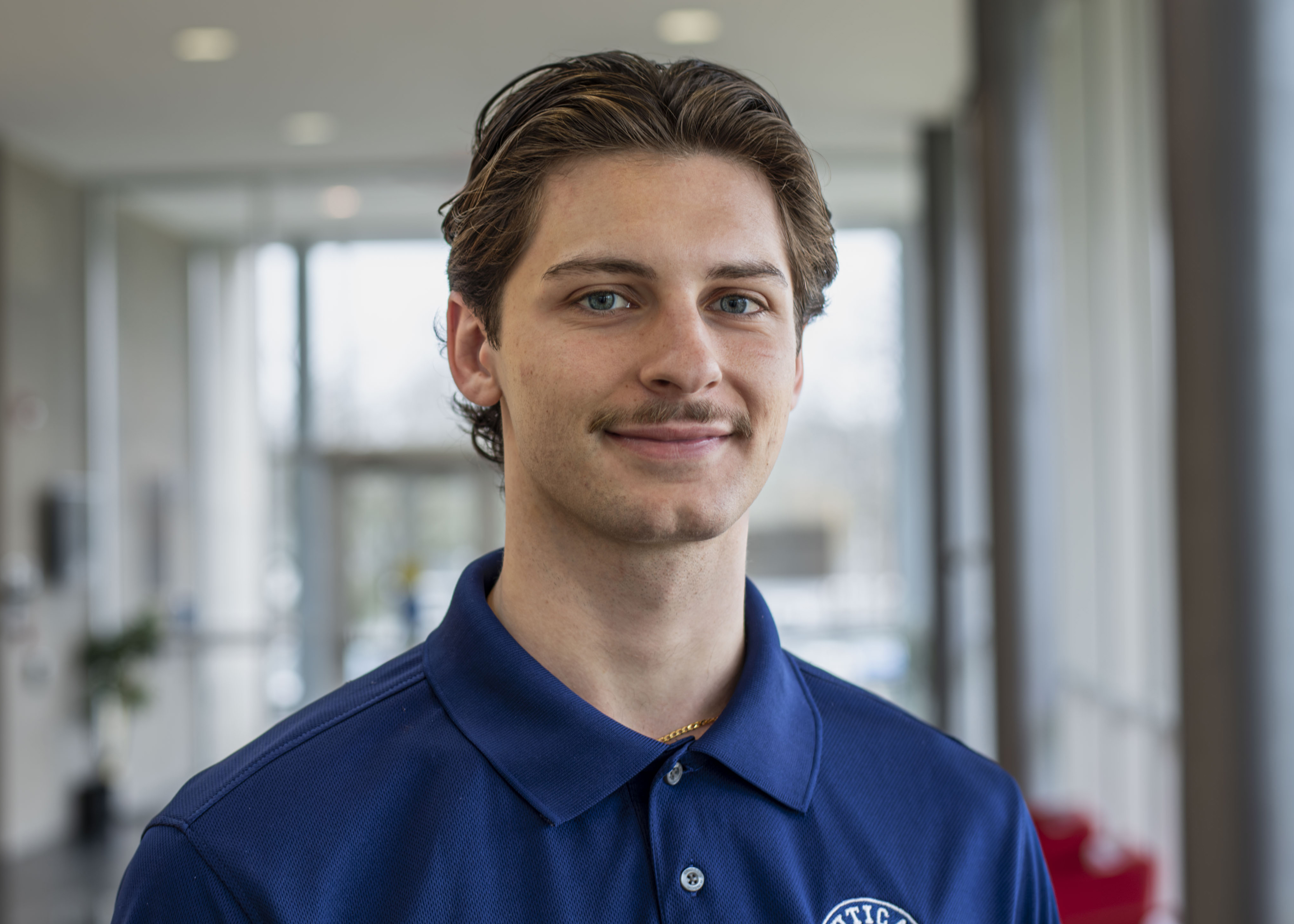 Eric Vitale in a blue shirt stands in a hallway of Bull Hall.