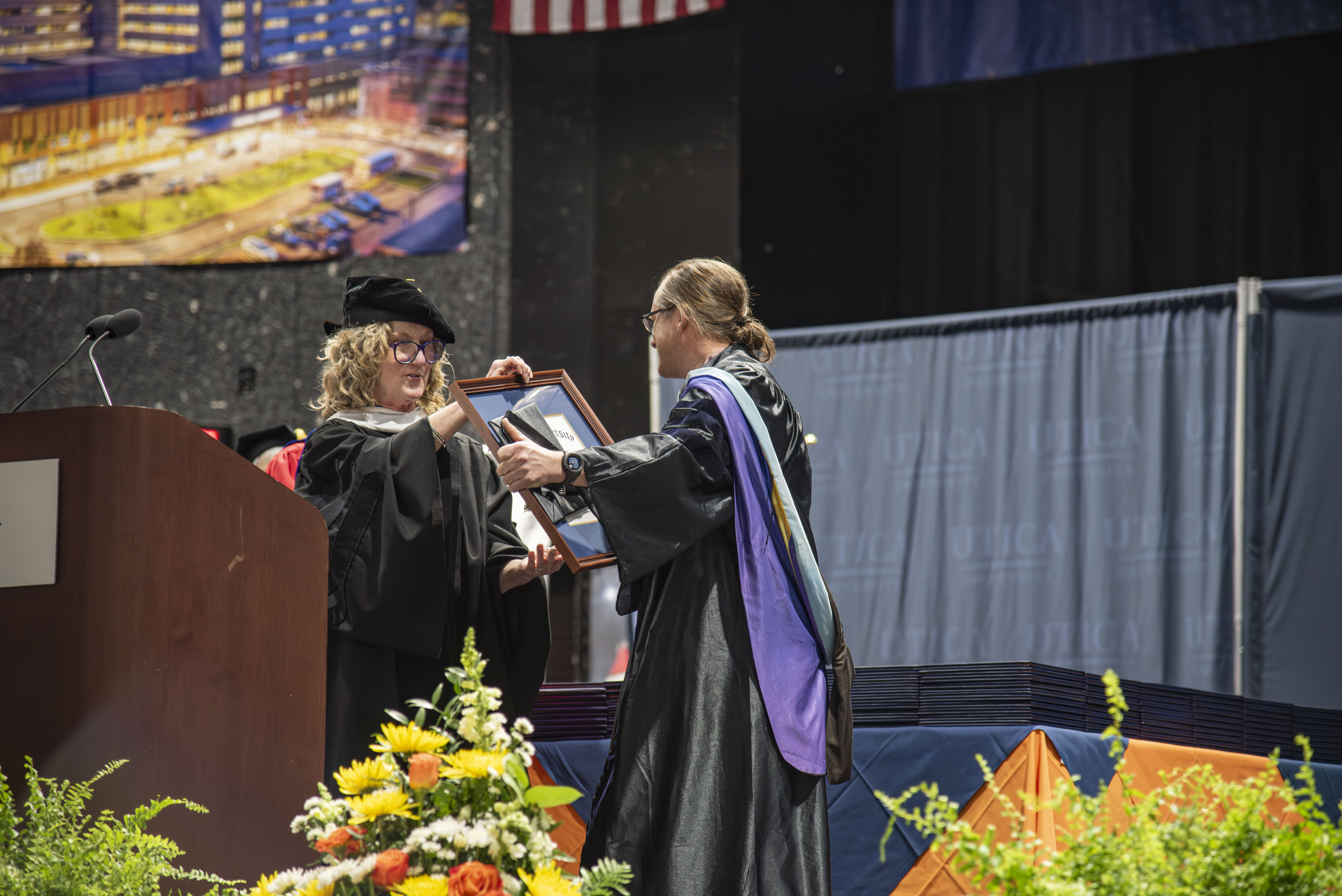 Beside a lectern, Provost Anne Damiano presents Professor Brad Emmons with the Crisafulli Award at the 2026 Commencement Ceremony.