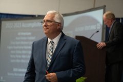 Jason Powles in blue suit hosts the Pioneer Hall of Fame Ceremony in May 2023.