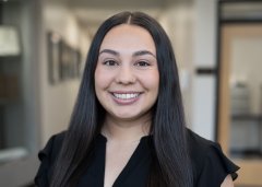 Megan White, with long dark hair and a black top, smiles at the camera.