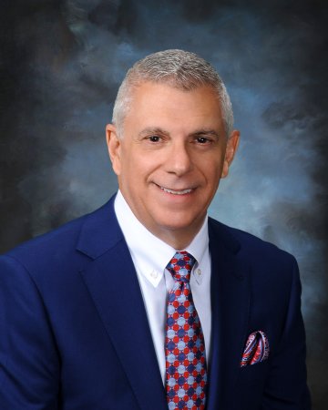 Anthony Picente in blue suit, white shirt and burgundy patterned tie, smiles.