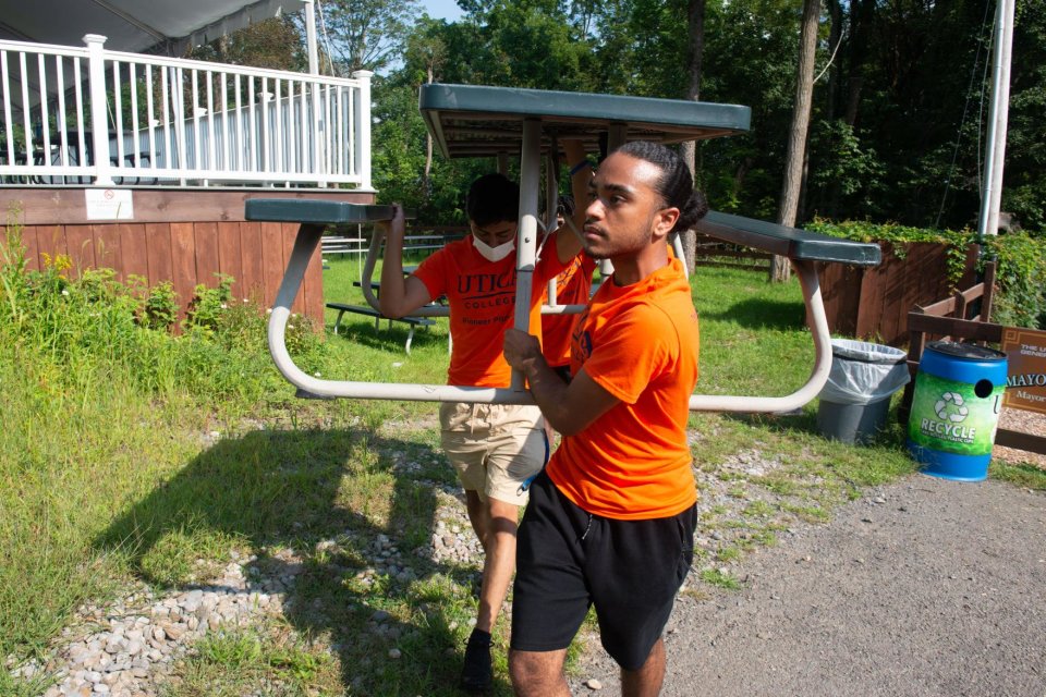 New Utica College students carry a picnic table on the grounds of the Utica Zoo as part of Pioneer Pitch-In.